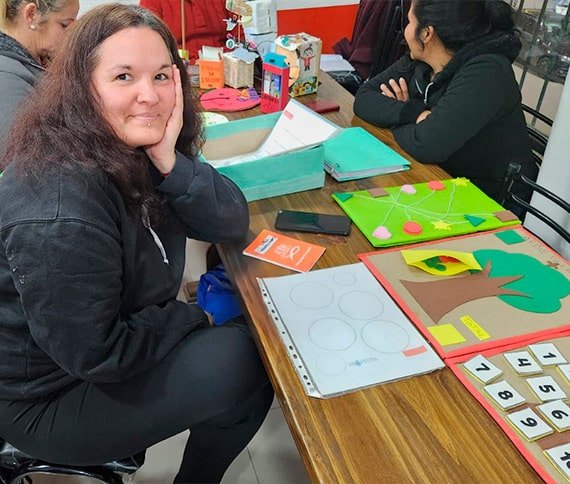 Mesa con materiales educativos y artesanías, incluyendo un folleto rojo, un teléfono negro y una caja verde.