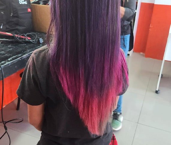 Cabello liso teñido en un degradado de colores, comenzando con morado oscuro en las raíces, rosa en el centro y durazno claro en las puntas.