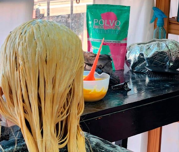 La imagen muestra la parte posterior de la cabeza de una persona cuyo cabello está siendo tratado con un producto para decoloración o tintura.