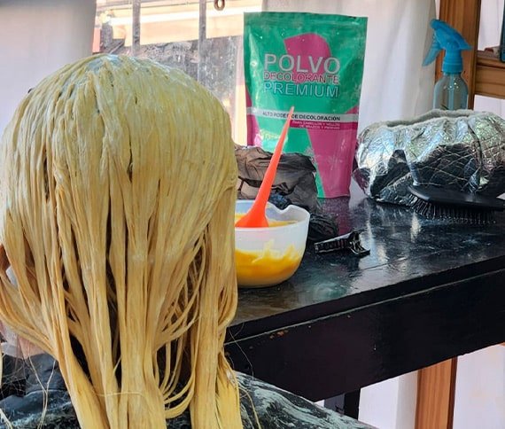 La imagen muestra la parte posterior de la cabeza de una persona cuyo cabello está siendo tratado con un producto para decoloración o tintura.