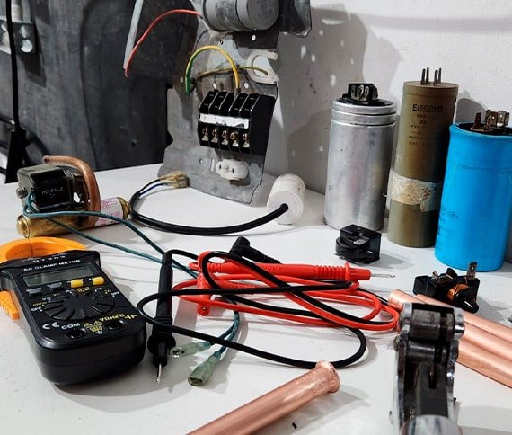 Personas trabajando en un proyecto de reparación electrónica sobre una mesa con herramientas y componentes.